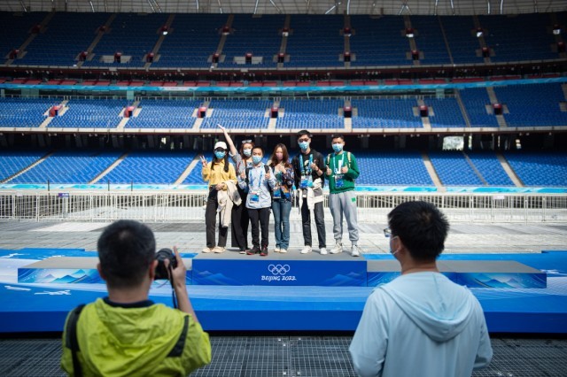 4月20日，受邀体验“双奥”主题旅游线路的北京冬奥会开闭幕式志愿者在滑板造型颁奖台上合影。